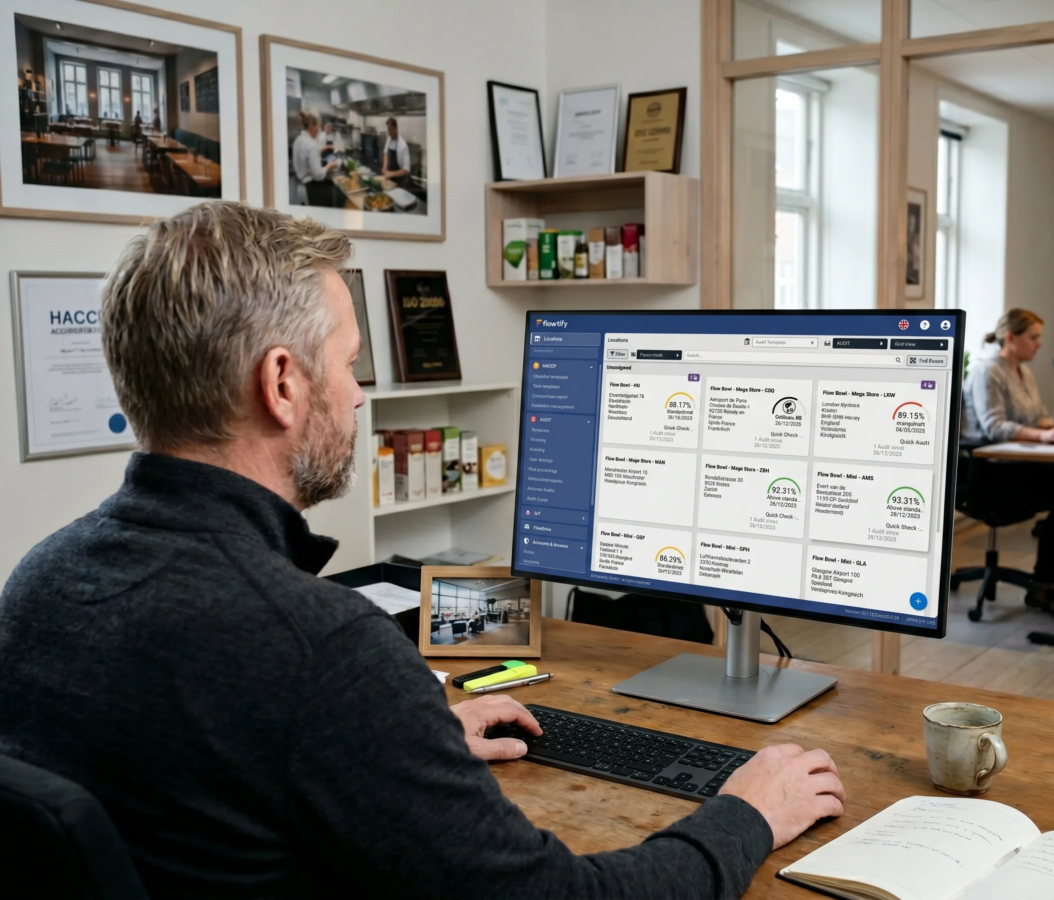 Senior quality director at the headquarters of a foodservice holding evaluating audit scores from multiple international locations in the flowtify grid view on a desktop monitor.