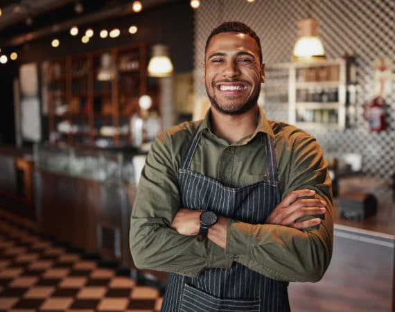 Afro-american cafe owner standing smiling wearing apron with folded arms