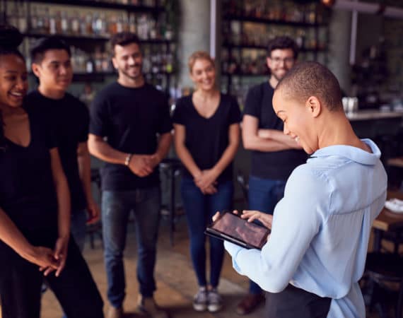 Female Restaurant Manager With Digital Tablet Giving Team Talk To Waiting Staff